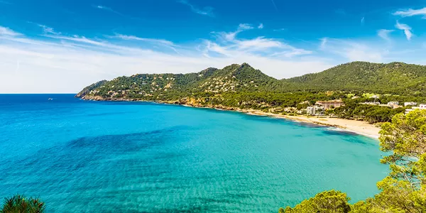 Küste von Mallorca mit blauem Meer, Sandstrand und grünen Hügeln unter blauem Himmel