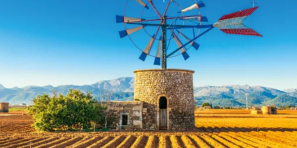 Traditionelle Windmühle aus Stein vor Bergen auf Mallorca unter klarem Himmel