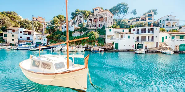 Segelboot vor Häusern am Wasser in einer Bucht auf Mallorca