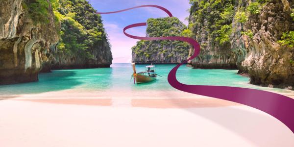 Türkisfarbenes Meer mit traditionellem Holzboot und steilen Felsen im Hintergrund, Strand mit rosa Sand