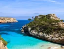 Felsige Küste mit Pinien und klarem blauem Wasser auf Mallorca unter blauem Himmel