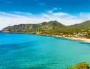 Küste von Mallorca mit blauem Meer, Sandstrand und grünen Hügeln unter blauem Himmel