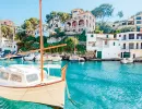 Segelboot vor Häusern am Wasser in einer Bucht auf Mallorca