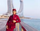 Crewmitglied bei Qatar Airways in roter Uniform steht am Geländer mit Blick auf Wasser und Stadt im Hintergrund