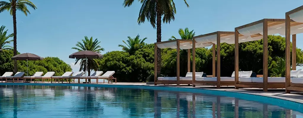 Sarena de Muro Resort Mallorca mit Poolbereich, Bali-Betten und Palmen unter blauem Himmel