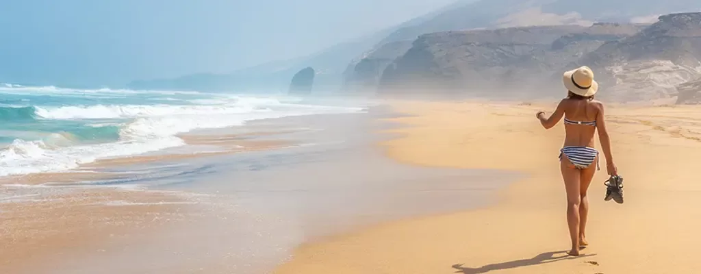 Kanareninsel Frau läuft am goldfarbenen Sandstrand mit Vulkanlandschaft im Hintergrund. Links sieht man wie die schäumenden Wellen des Meeres den Strand erreichen